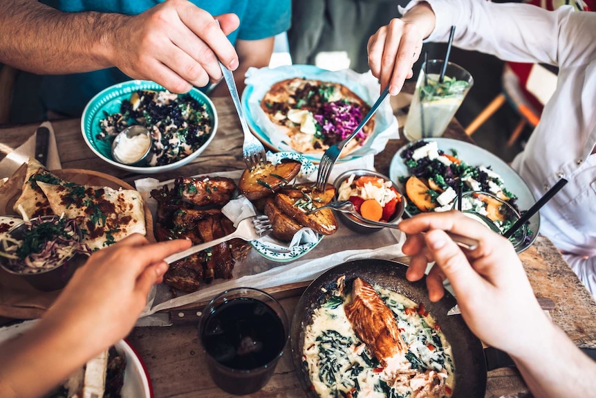 Bird's eye food of a group of people eating baked salmon, pita, and roast vegetables in a restaurant.