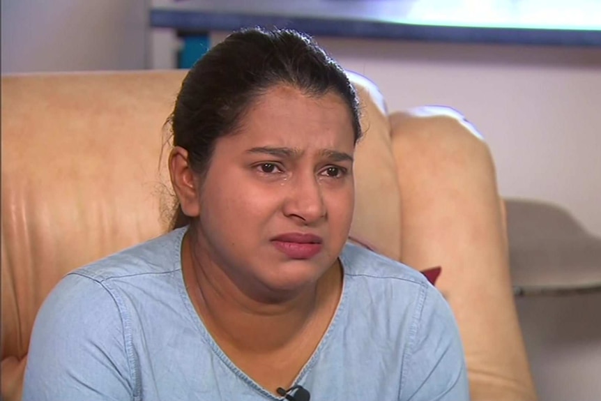 A woman in a blue shirt cries sitting on a leather couch.