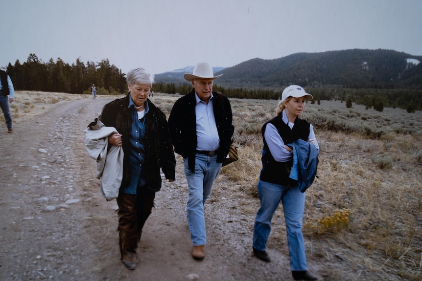 Three people in jeans and cowboy boots walk down a dirt path 