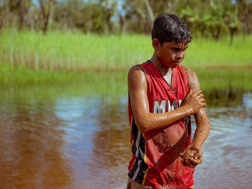 Junior rubs mud into his skin.