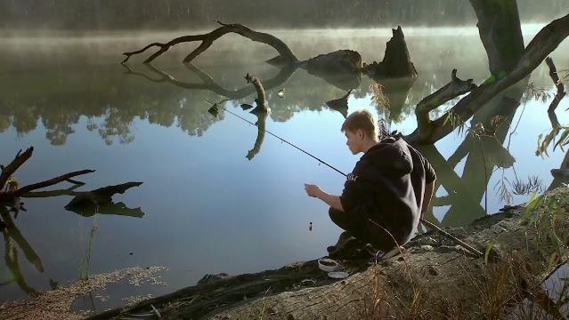 Boy fishes with rod at edge of a river