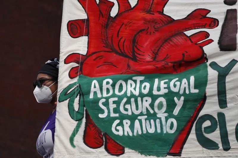 一个女人举着一个牌子，上面用西班牙语用绿色和红色写着， "合法、安全和免费的堕胎" 