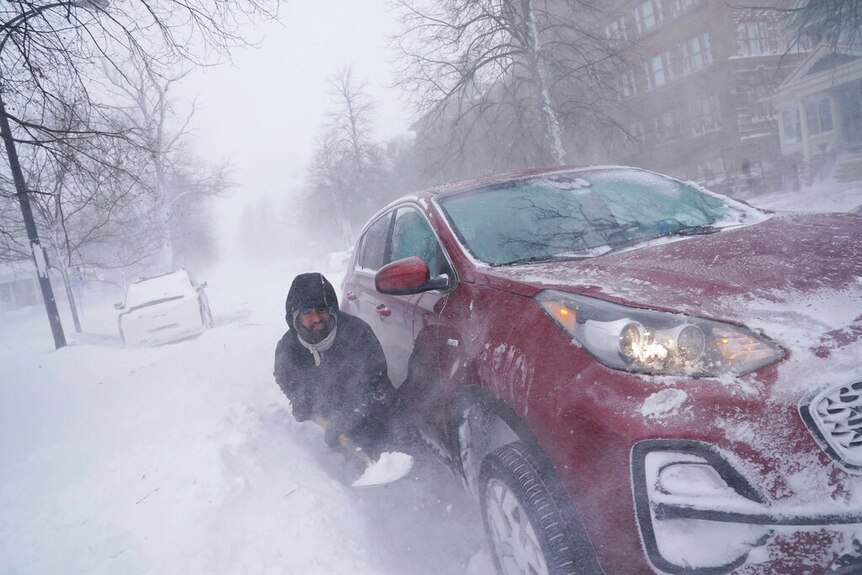 A man tries to dig out his car from the snow in New York.