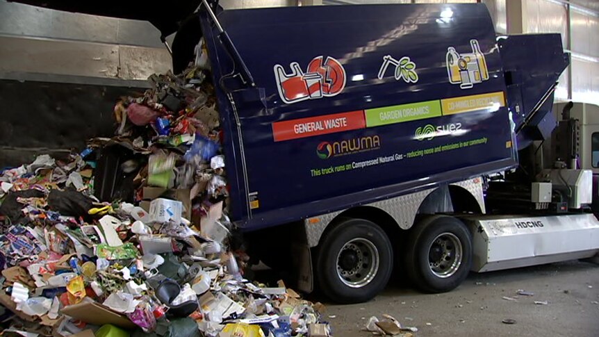 A garbage truck unloads rubbish in a warehouse