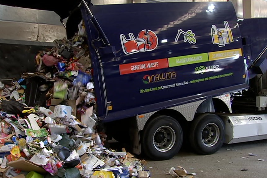 A garbage truck unloads rubbish in a warehouse