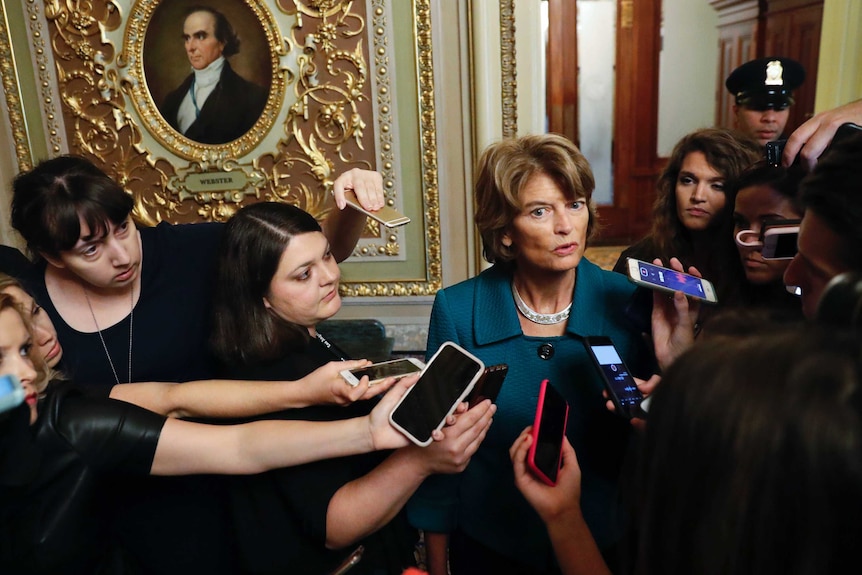 A Senator surrounded by journalists.
