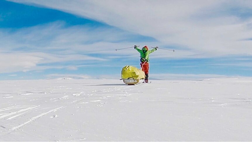 Colin O'Brady holds his ski poles in the air as he stands near his sled in the ice.