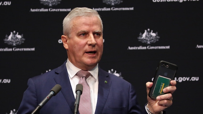 Michael McCormack looks at his phone while standing at a podium.