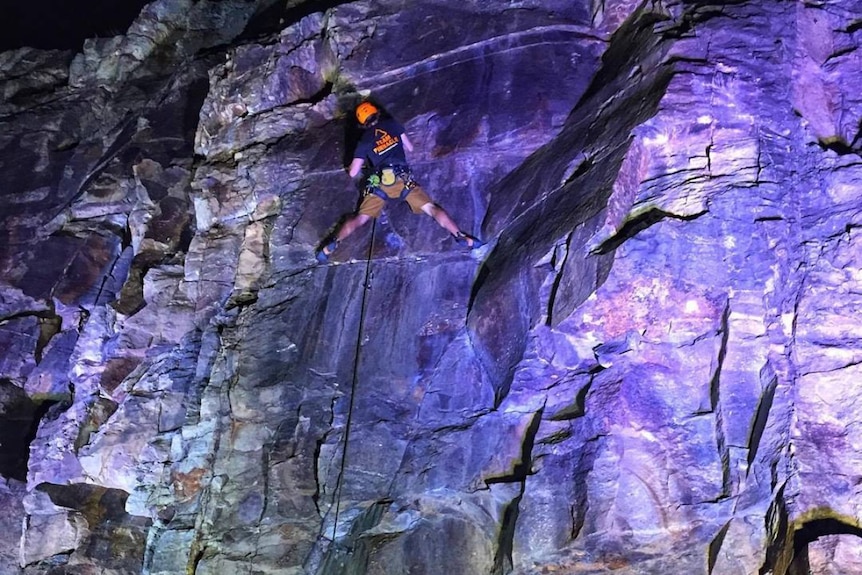 Josh Worley climbing the purple-lit rock wall at Brisbane's Kangaroo Point cliffs.