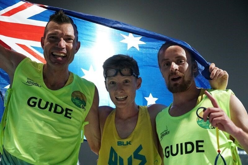 Three men in running gear stand in front of an Australian flag.