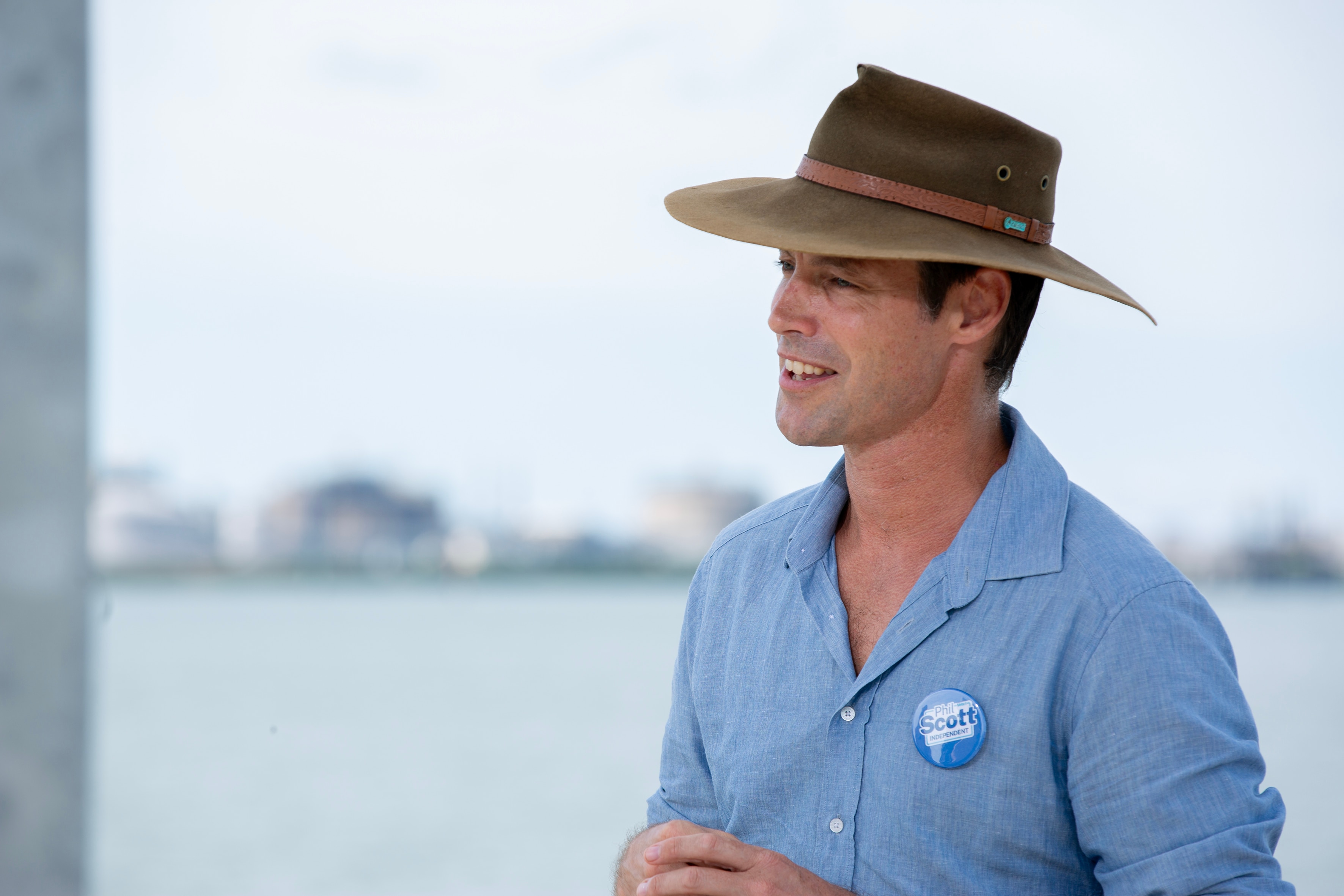 Un hombre con camisa azul y sombrero de ala ancha se encuentra frente al mar