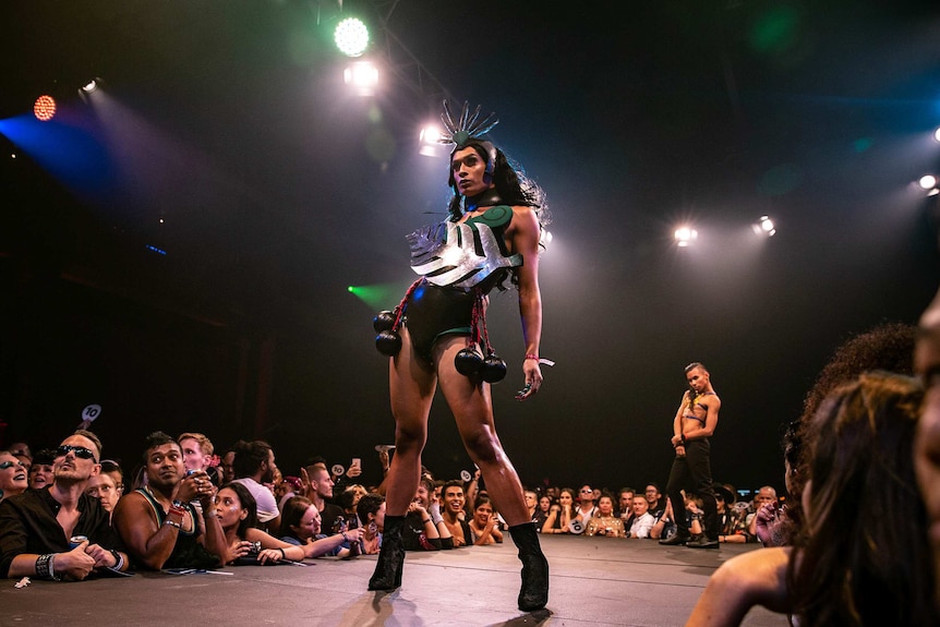 A vogue performer wearing a black-and-green outfit with a prominent silver fern poses on the runway at Sissy Ball 2019.