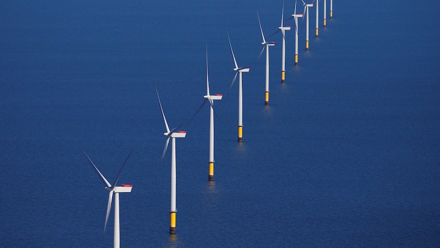 A long line of wind turbines in the middle of the ocean.