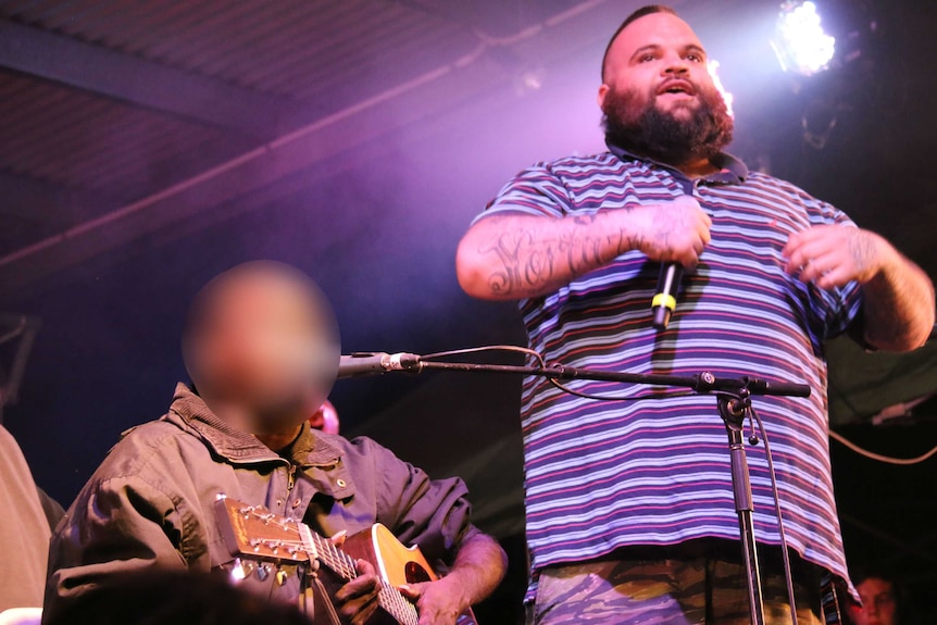 Dr G Yunupingu sits and plays guitar on stage while Briggs performs standing.