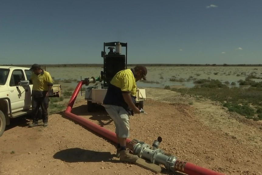 Two workers inspect a pump, bringing water in a pipe out of a lake.