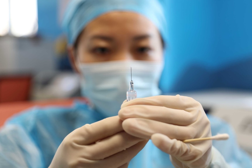 A female health worker holds a syringe in front of her face