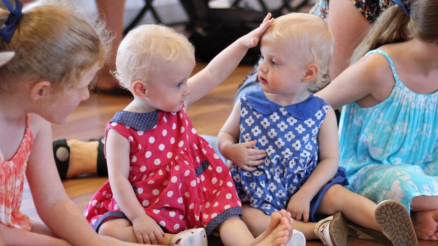 A blonde baby touches the head of her twin sister