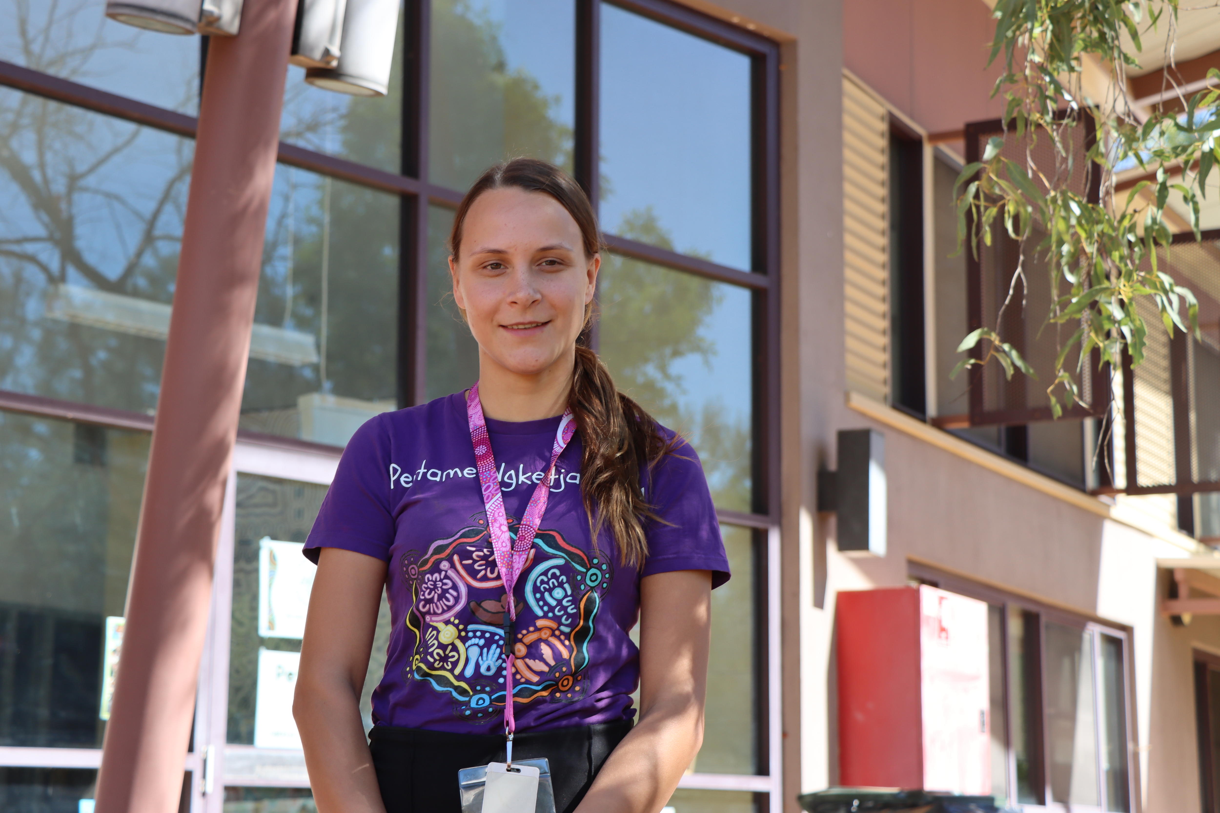 A woman in a purple shirt looks into the camera.
