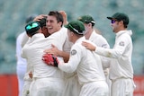 Patrick Cummins in the middle being hugged by team-mates after first Test wicket