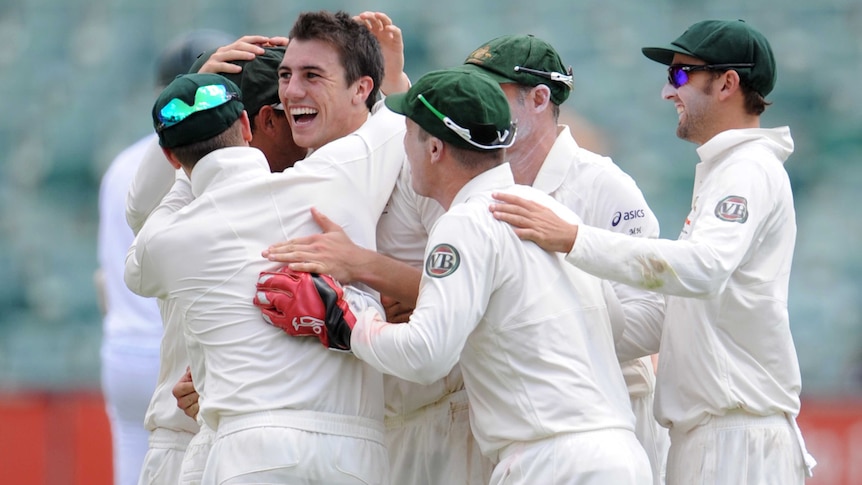 Patrick Cummins in the middle being hugged by team-mates after first Test wicket