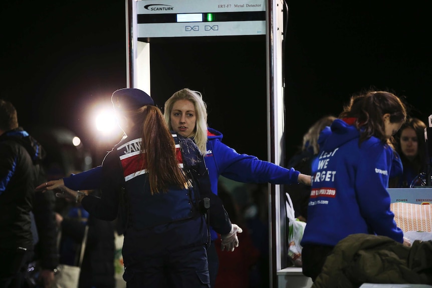 A women wearing a hoodie holds her arms out wide as she is checked by a police officer.