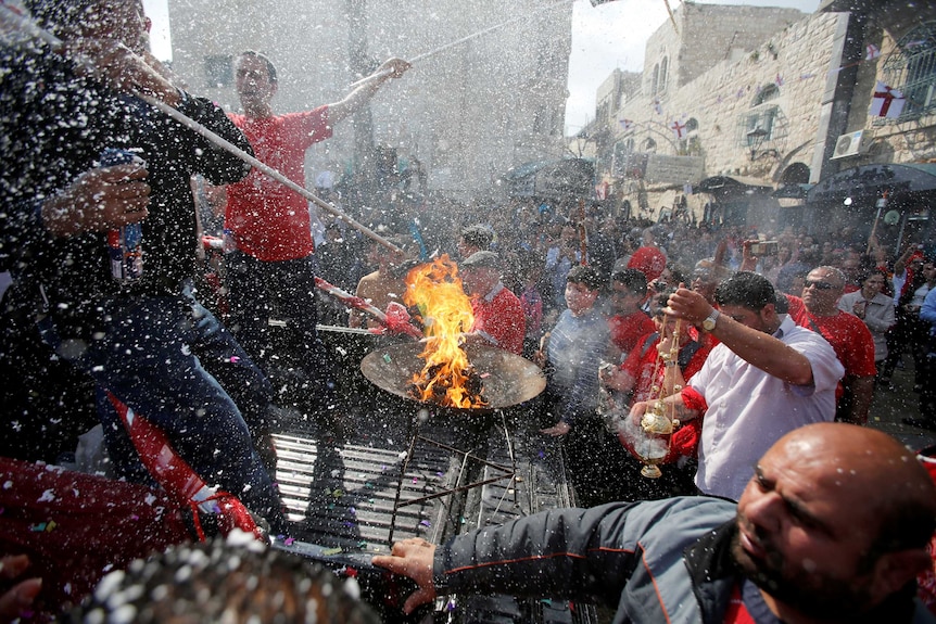 Hundreds of people wearing red and white fill the streets of jeruslam, a fire burns in the centre of the frame.