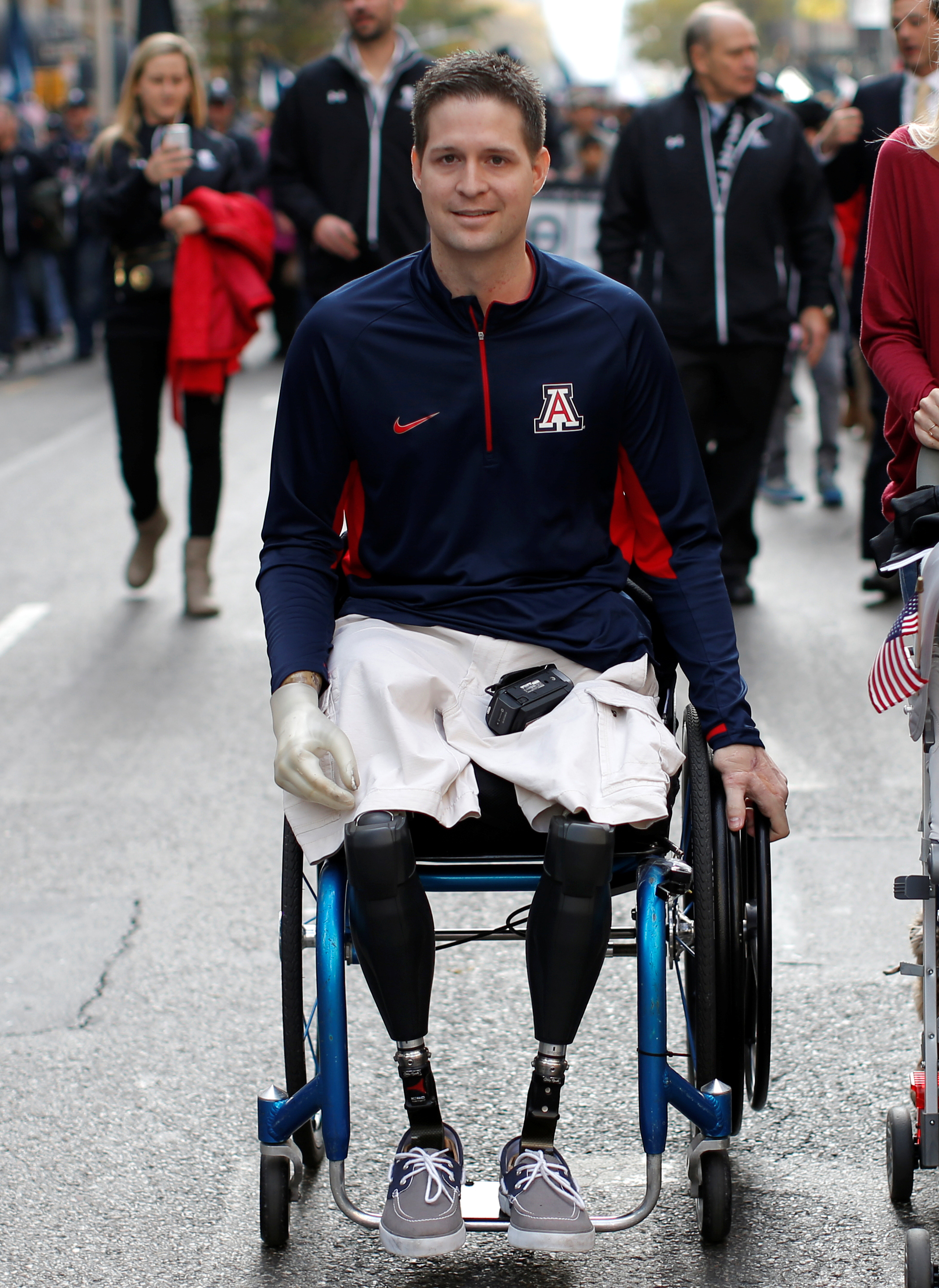 A triple amputee wheels himself in a parade with his one available hand.