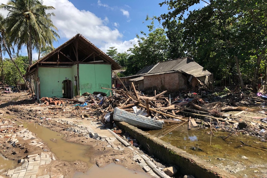 A mattress lies among rubble and pooled water in damaged houses.