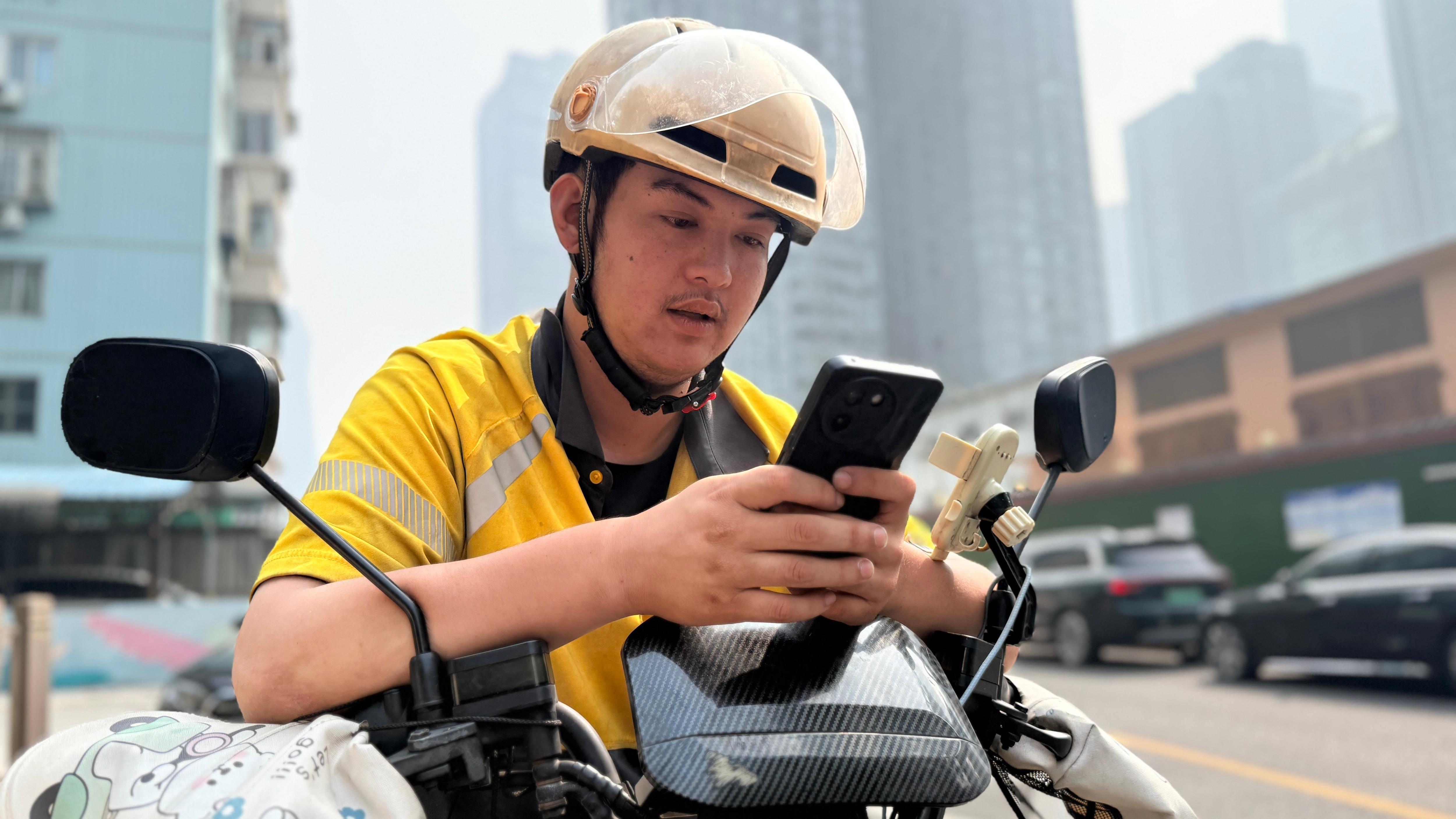 A young man in a bright yellow jacket looks intently at his mobile phone.
