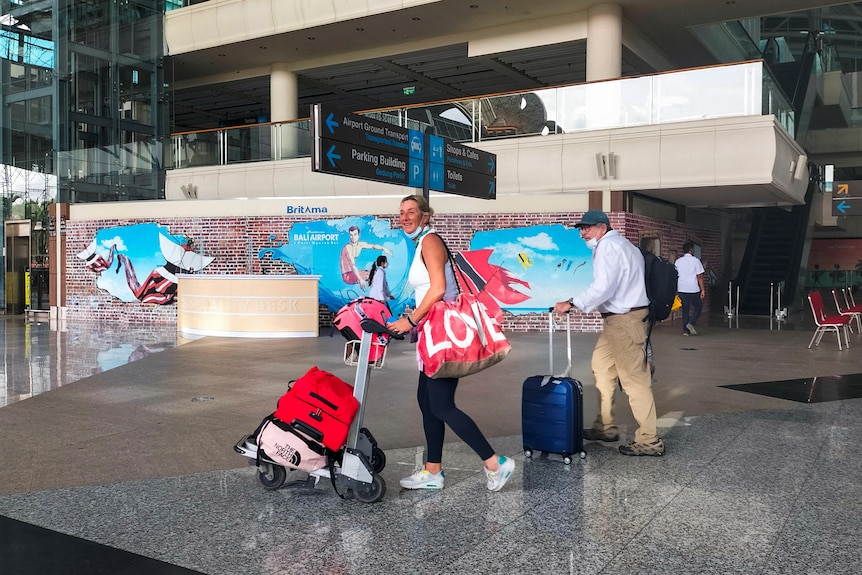 Foreign tourists carrying their luggage walk as they arrive at Bali airport