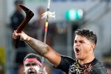 Latrell Mitchell stands and shouts while surrounded by kneeling Indigenous All Stars during a war cry.