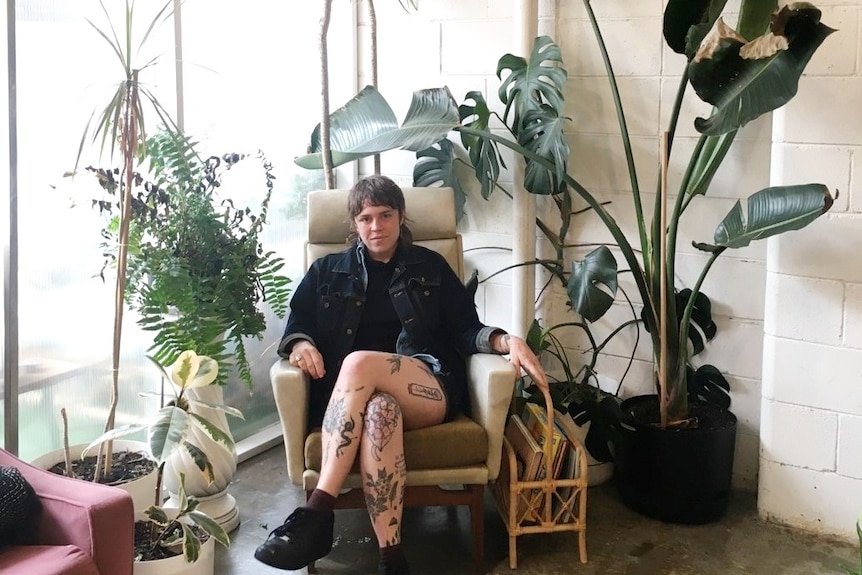 Woman sits among her indoor plant collection in a studio, a committed plant parent.