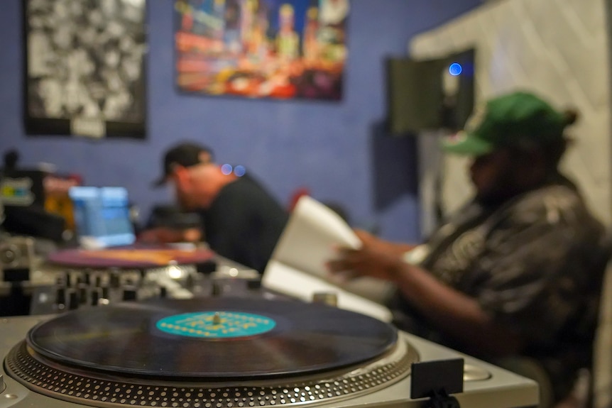 A blurry photo of a man and an Aboriginal teen sitting in a studio, with a record player in the foreground