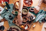 A hand reaches across a table full of cheese, dip, cured meat and other snack foods to pick a snack. 