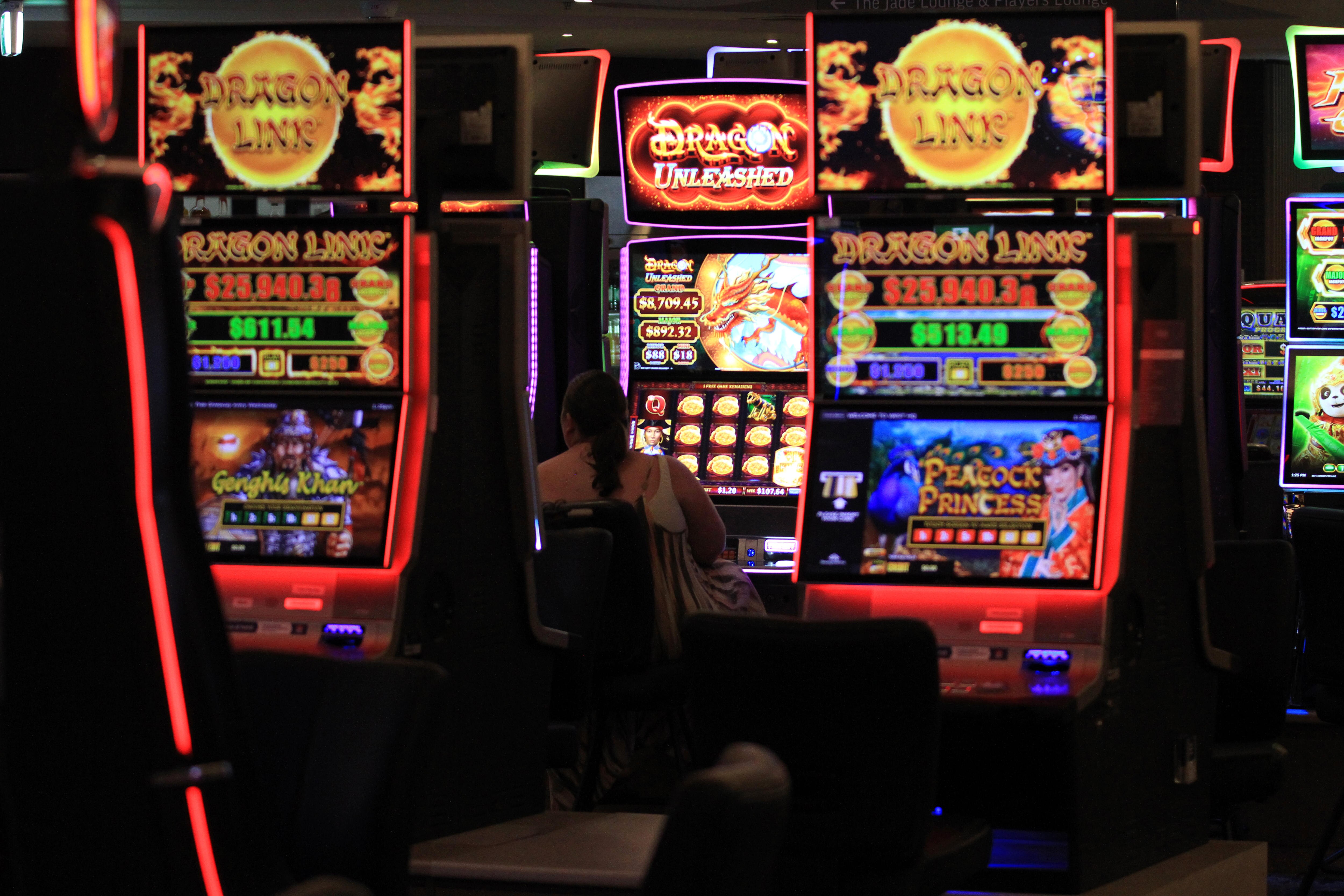 A woman sits at a poker machine. Surrounding her are several large, bright and colourfully lit machines.
