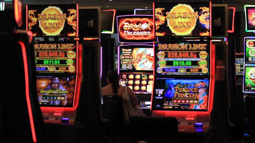 A woman sits at a poker machine. Surrounding her are several large, bright and colourfully lit machines.
