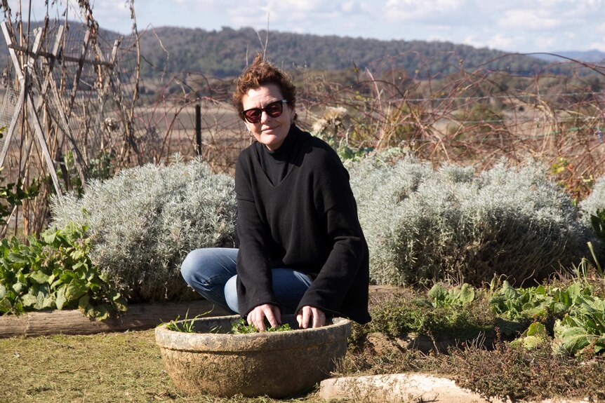 A woman squatting next to a pot of herbs in a kitchen garden
