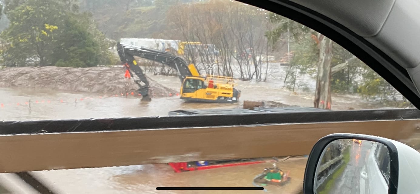 Excavator machine in floodwaters, photo taken from a car.