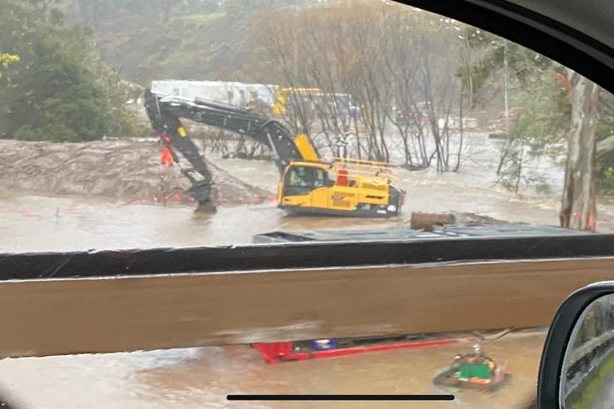 Excavator machine in floodwaters, photo taken from a car.