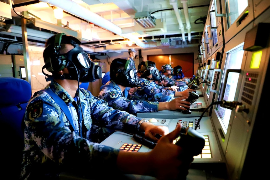 Sailors wearing gas masks operate a combat direction system console aboard the amphibious dock landing ship Changbaishan.