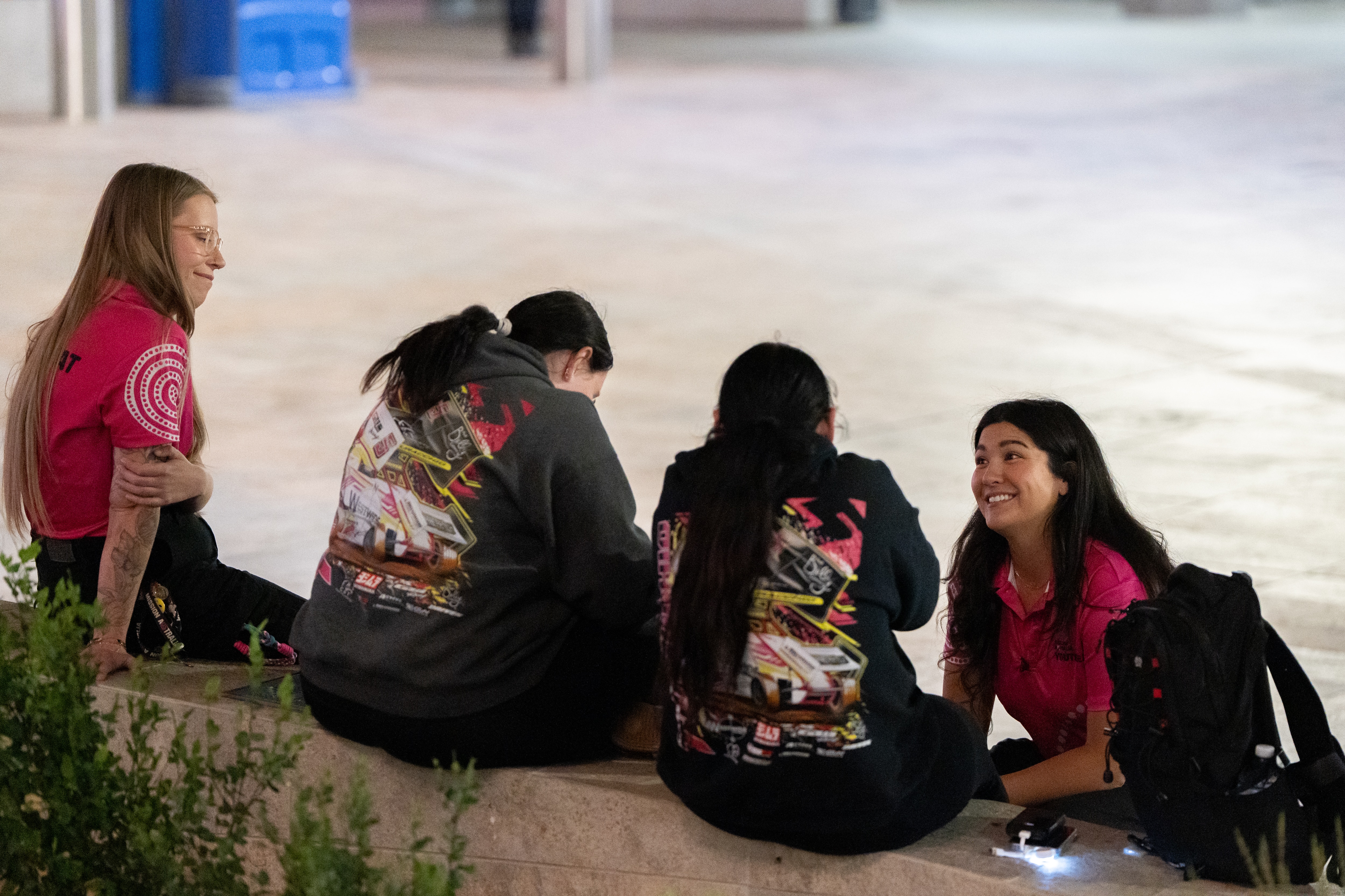 Two youth workers chat to two young women sitting on a pavement.
