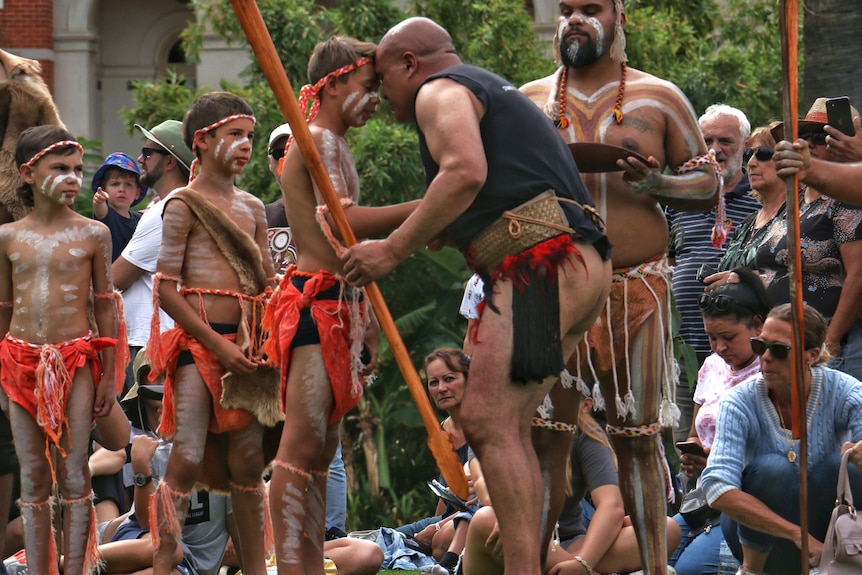 A Māori man touches noses with an Indigenous young man as others look on.