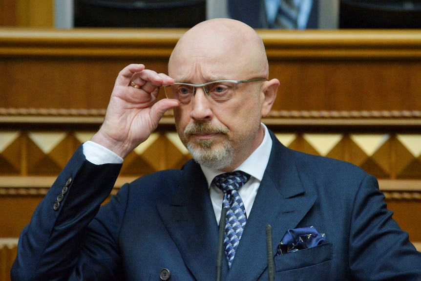 A man adjusts his glasses in a suit. 