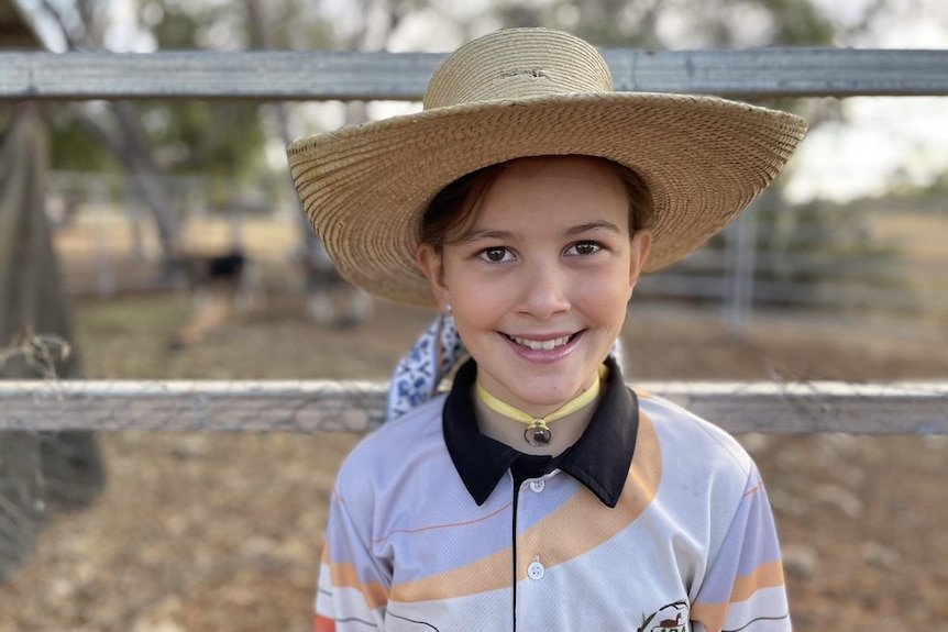 Jodie Muntelwit's daughter stands next to a fence wearing a large hat.