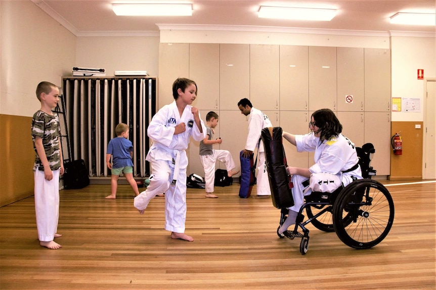 A woman sits in a wheelchair teaching martial arts to a group of kids.