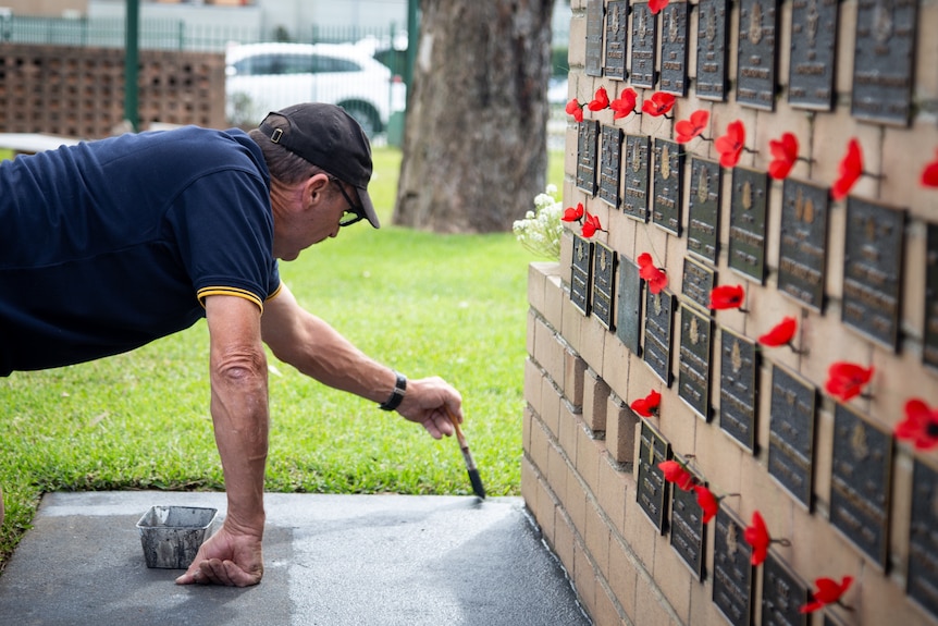 a man holding a paint brush on his hands and knees and painting the ground