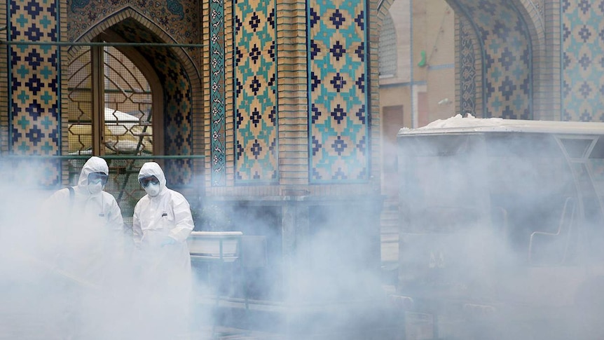 Disinfectant spray rises above workers in hazard suits in front of a religious shrine, in Iran.