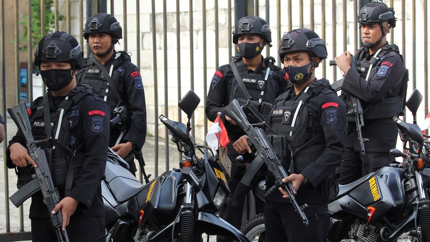 Armed motorcyle police officers stand guard in a tight group outside a courthouse.