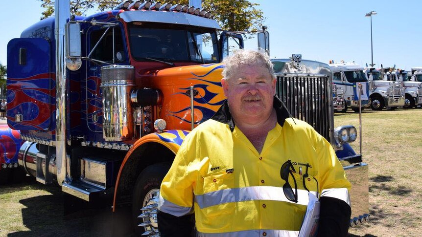 A man wearing high-vis in front of a large truck, painted purple with orange flames. 