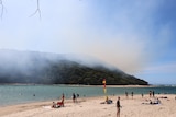 Beach in view with hill in background with smoke coming out from it. 